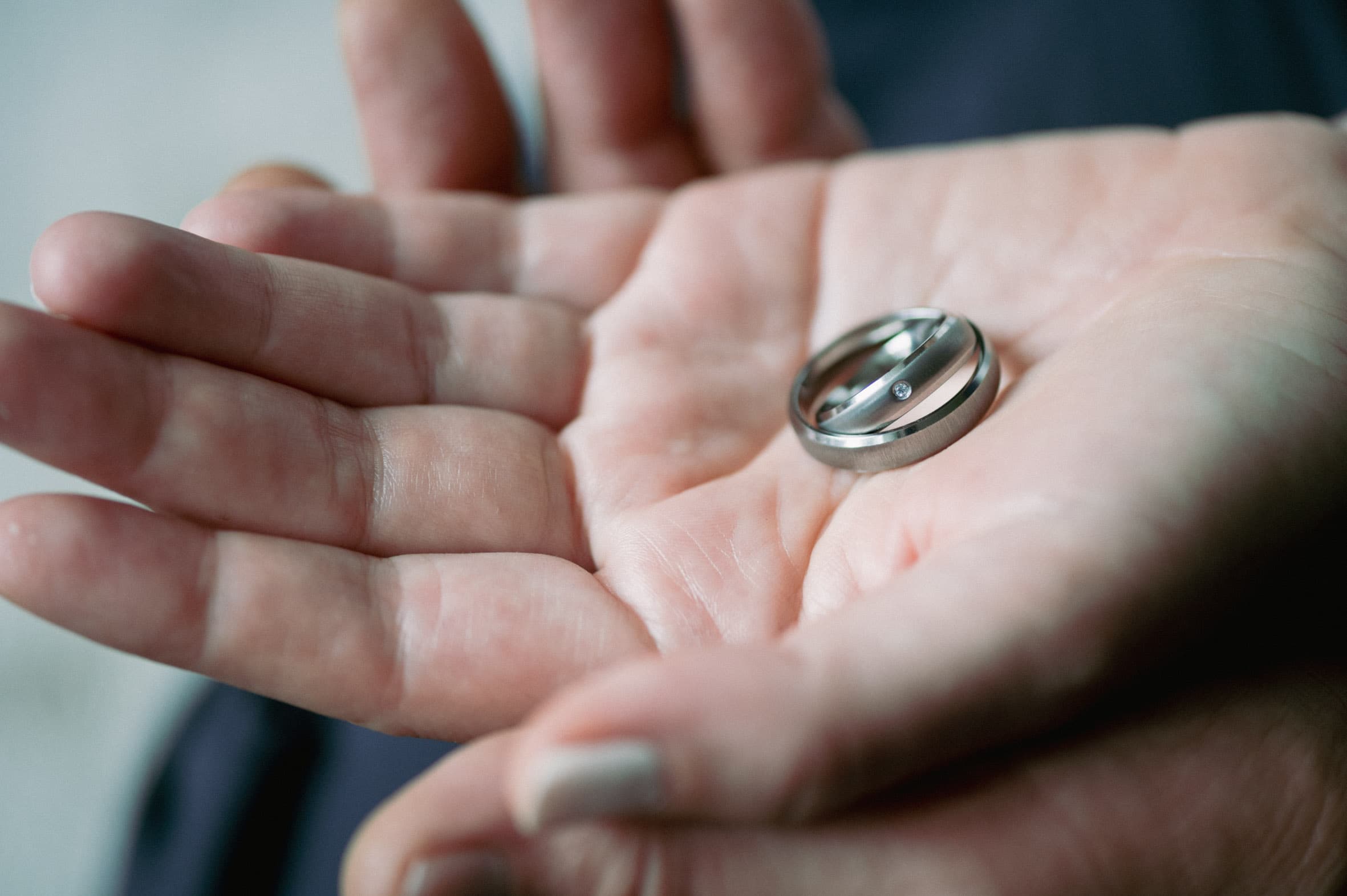 Zwei schlichte Titanringe von ReWi Titan liegen in einer geöffneten Hand, matt gebürstete Oberfläche mit feinem Diamantakzent als Symbol für Verbundenheit und Beständigkeit