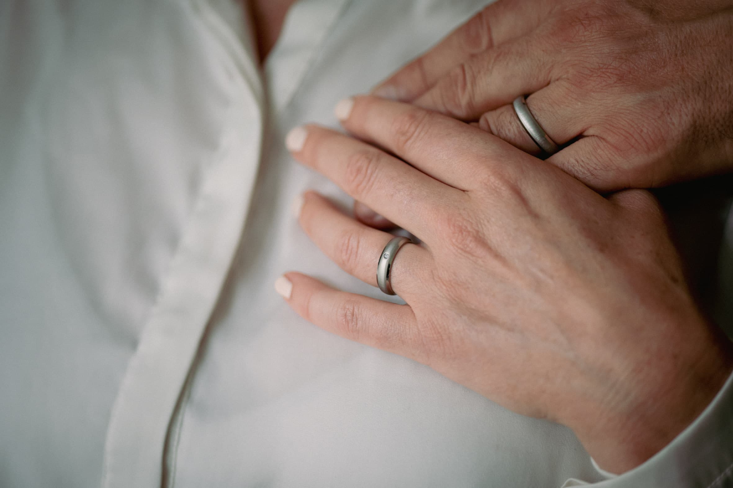 Zwei übereinanderliegende Hände mit schlichten Titanringen von ReWi Titan, matte Oberfläche mit dezentem Steinbesatz als Symbol für Partnerschaft und Beständigkeit