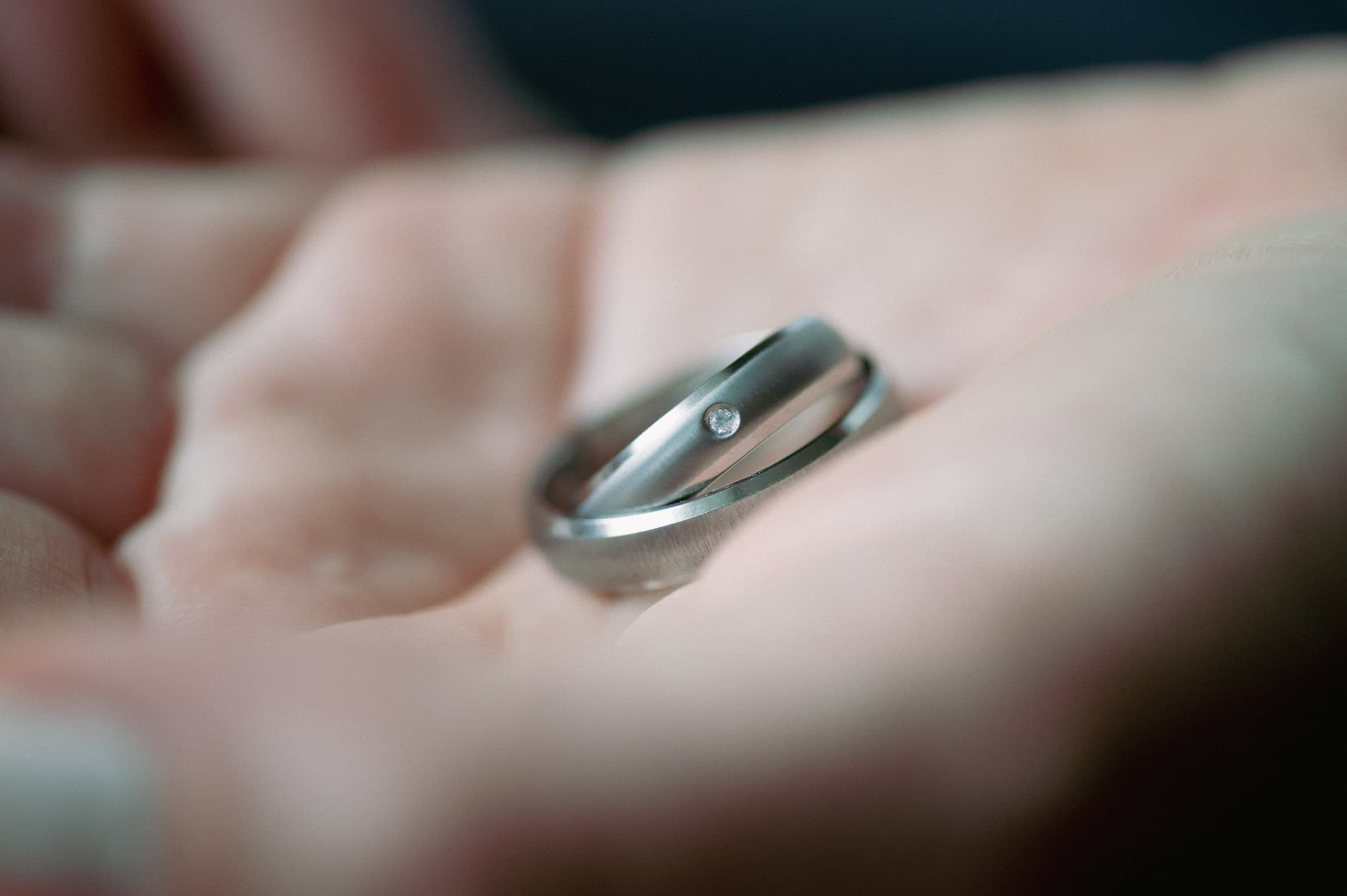 Nahaufnahme zweier übereinanderliegender Titanringe von ReWi Titan in einer geöffneten Hand, matte Oberfläche mit bündig gefasstem Diamanten und polierter Innenkante