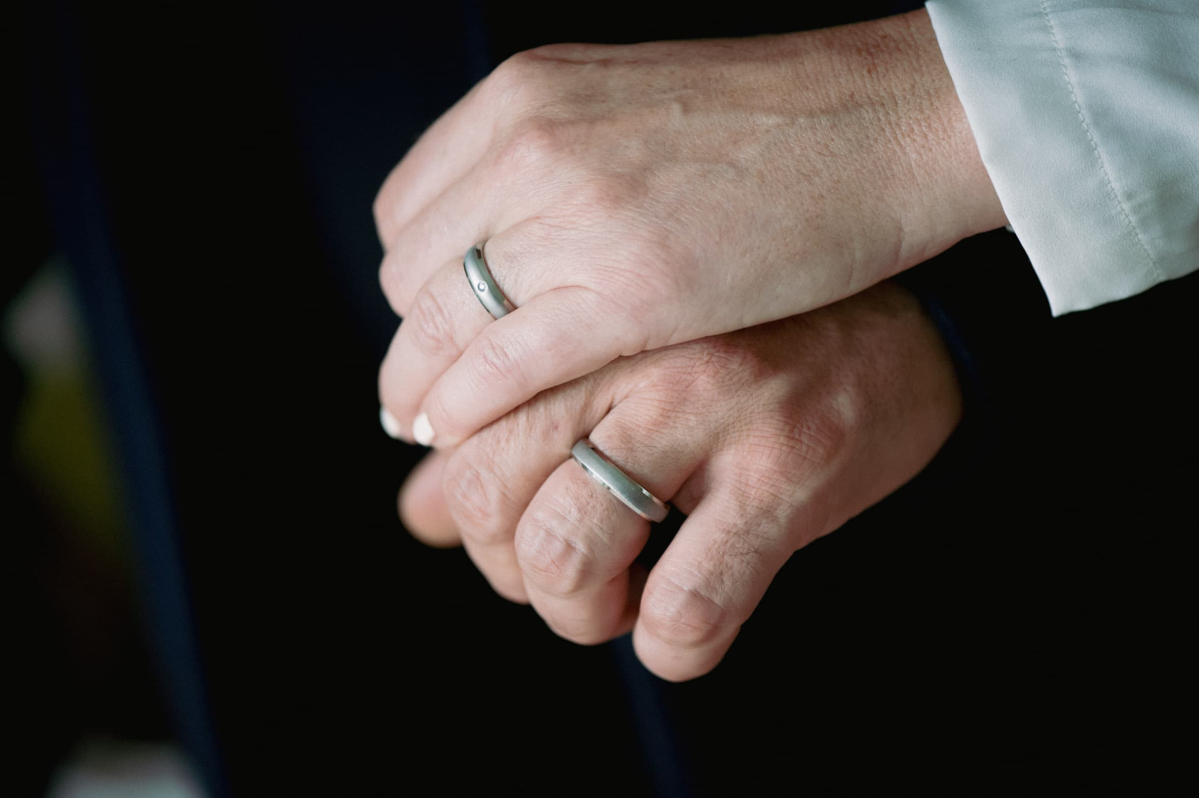 Ineinandergelegte Hände eines Paares mit schlichten Titanringen von ReWi Titan, matte Oberfläche mit dezentem Stein, getragen als Zeichen von Zusammenhalt und Verlässlichkeit