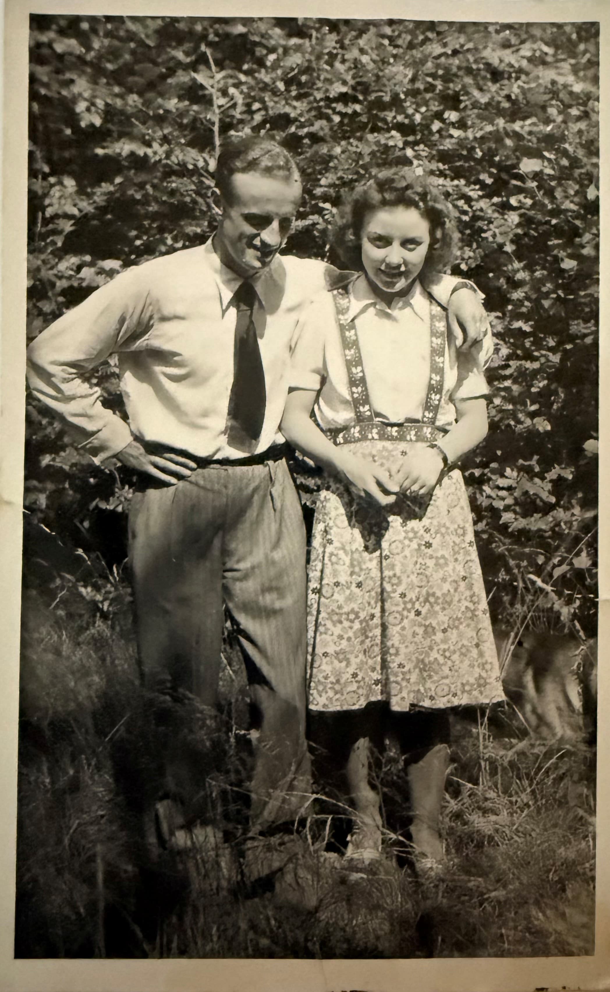 Historisches Schwarzweißfoto eines jungen Paares im Freien, Arm in Arm zwischen Bäumen stehend, als Sinnbild für Tradition und Generationen eines Berliner Familienbetriebs.