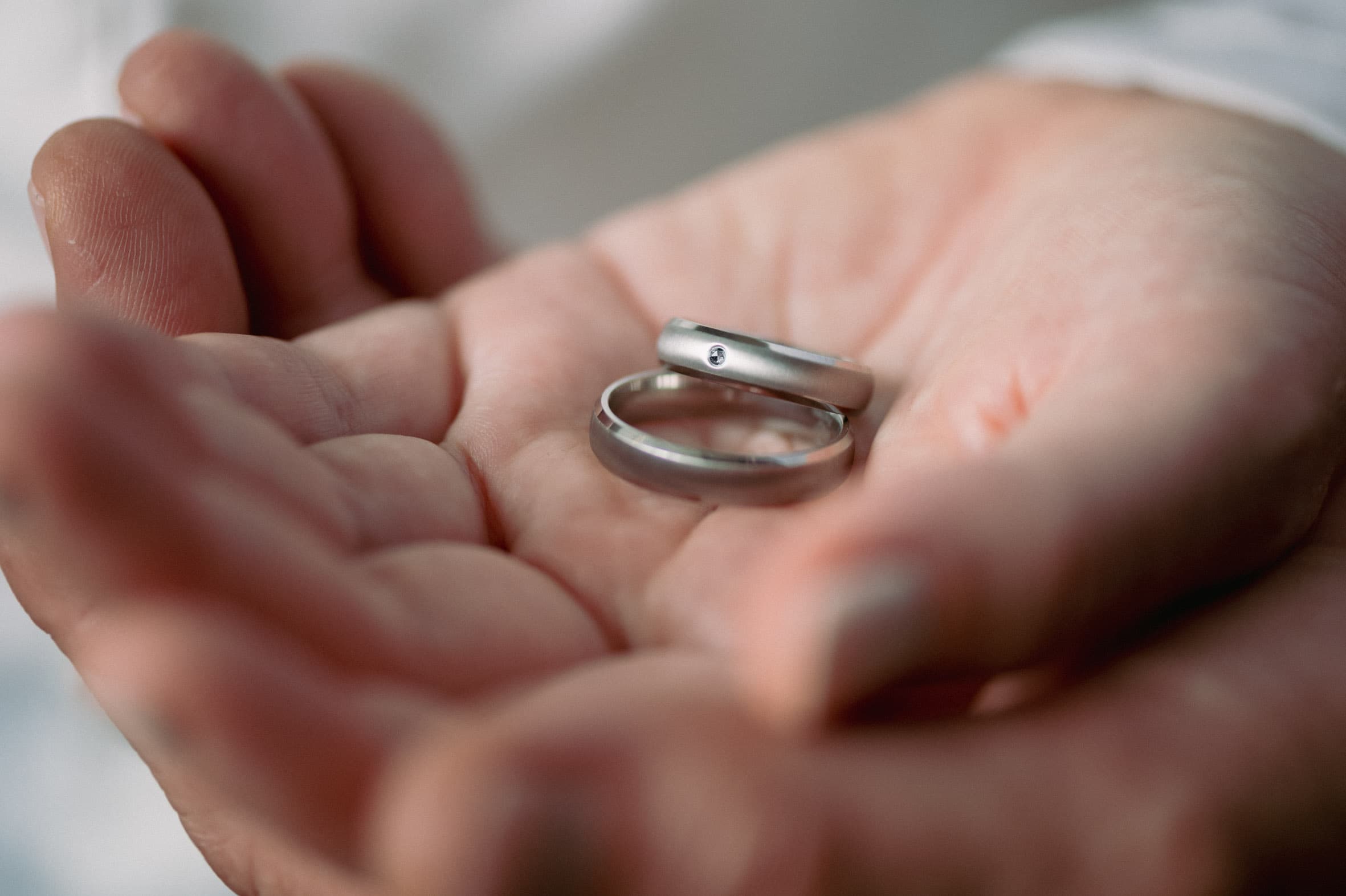 Zwei schlichte Titanringe in einer geöffneten Hand liegend, ein Ring mit kleinem Steinbesatz, ruhige Aufnahme als Symbol für Zusammenhalt und dauerhafte Verbindung.